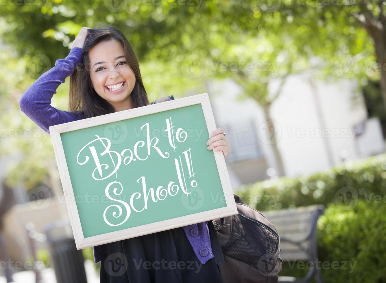 blandad lopp kvinna studerande innehav svarta tavlan med tillbaka till skola foto