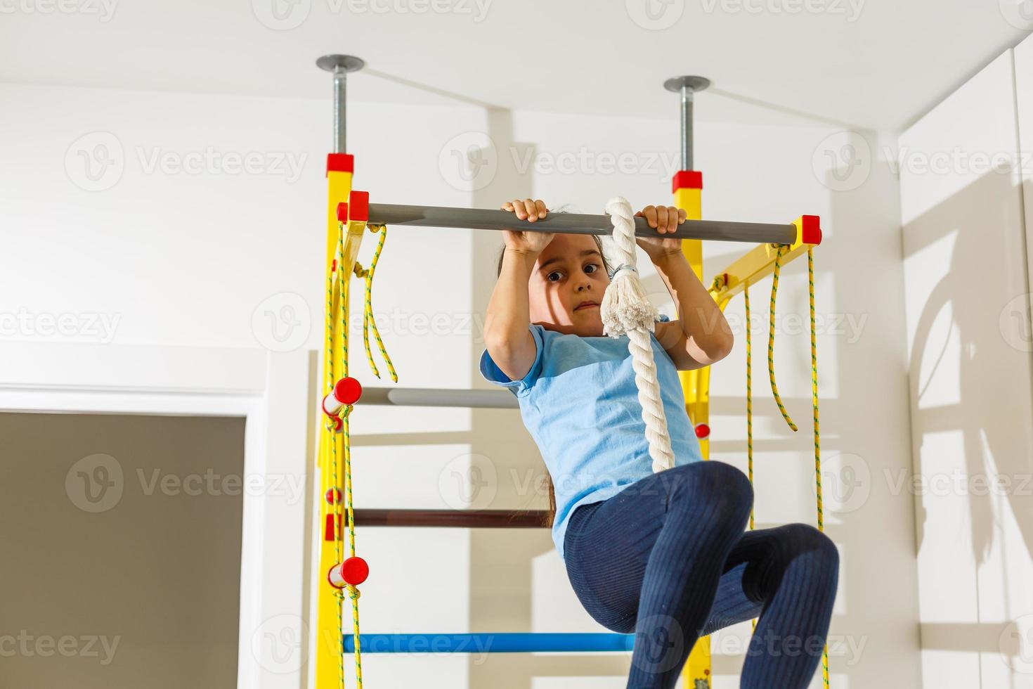 barn aktivitet begrepp. liten caucasian flicka har stretching övningar på vägg barer inomhus.horisontell bild sammansättning foto