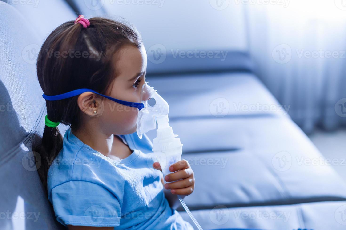 liten caucasian flicka är andas med särskild mask, som hjälper till sluta astma ge sig på eller lindra symptom av respiratorisk sjukdom. foto