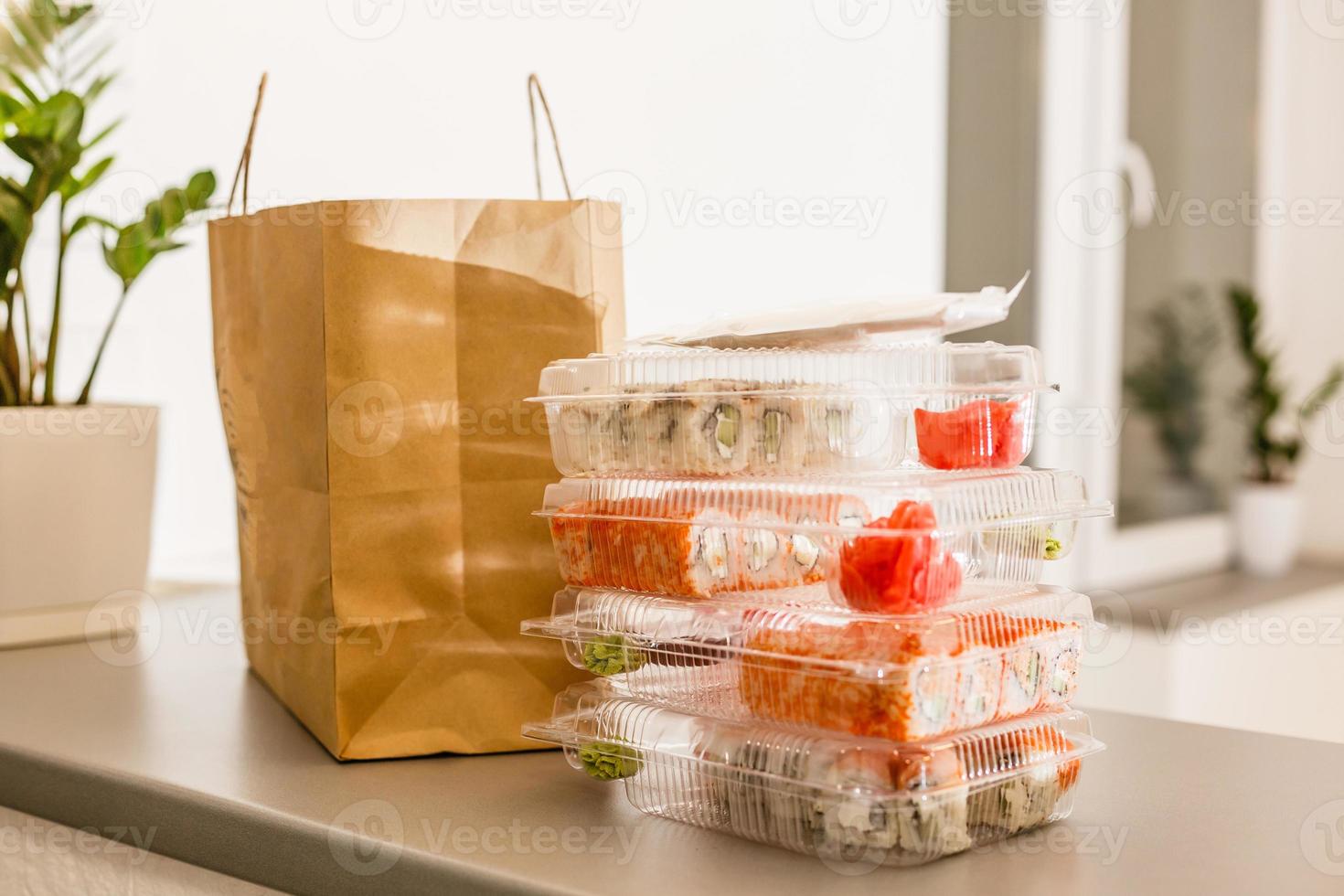 sushi rullar i plast låda nära papper paket på vit tabell. leverans. ta bort. foto