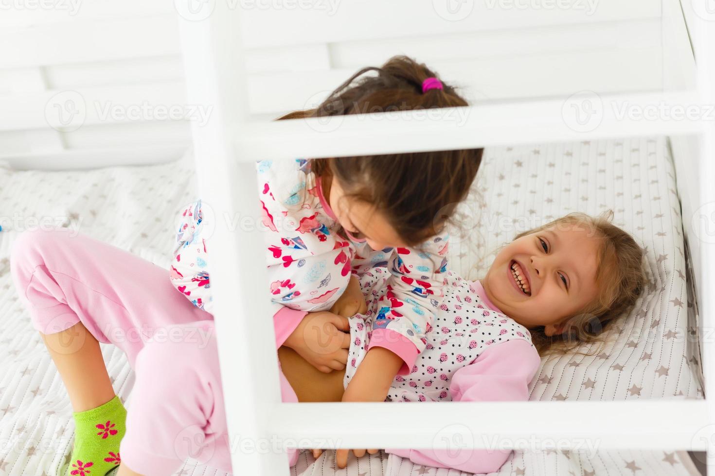 två flickor i pyjamas Sammanträde på säng foto