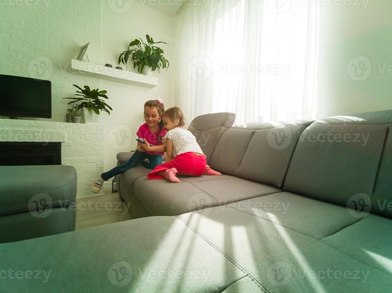 två barn med prylar. syster och bror delning rolig innehåll på smartphone och digital läsplatta på soffa på Hem. familj vänskap och kommunikation begrepp foto