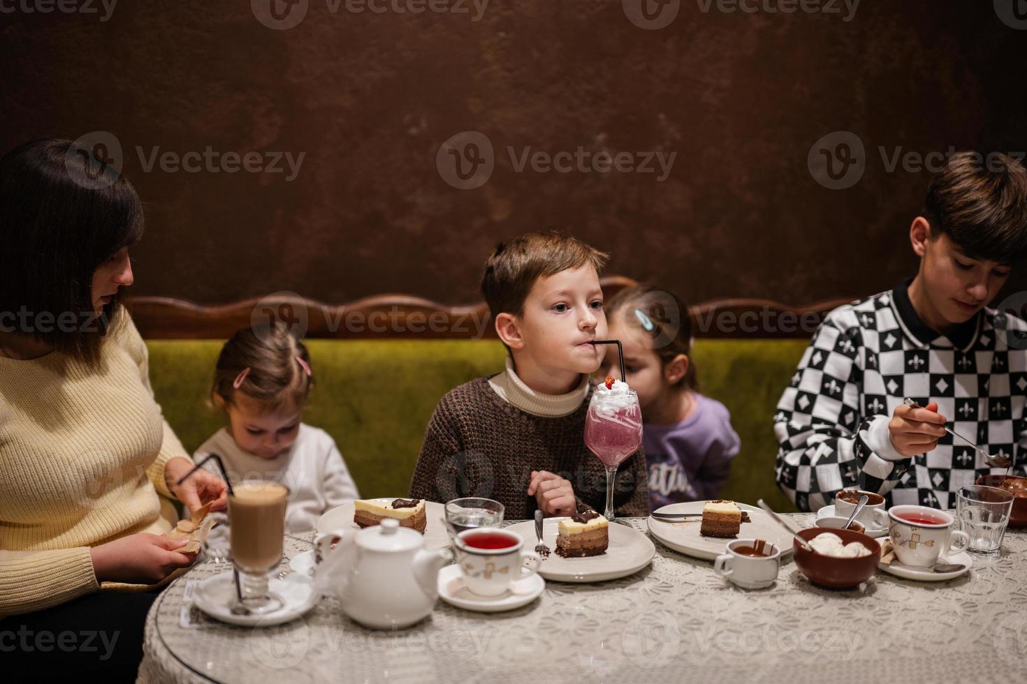 Lycklig familj äter desserter tillsammans på mysigt Kafé och har roligt. pojke unge dryck mjölk skaka. foto