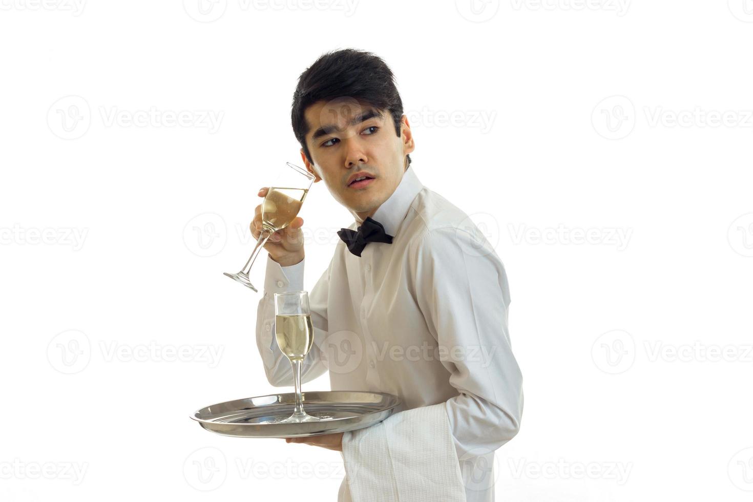 fantastisk ung servitör i en skjorta innehav en glas av vin och ser mot de foto
