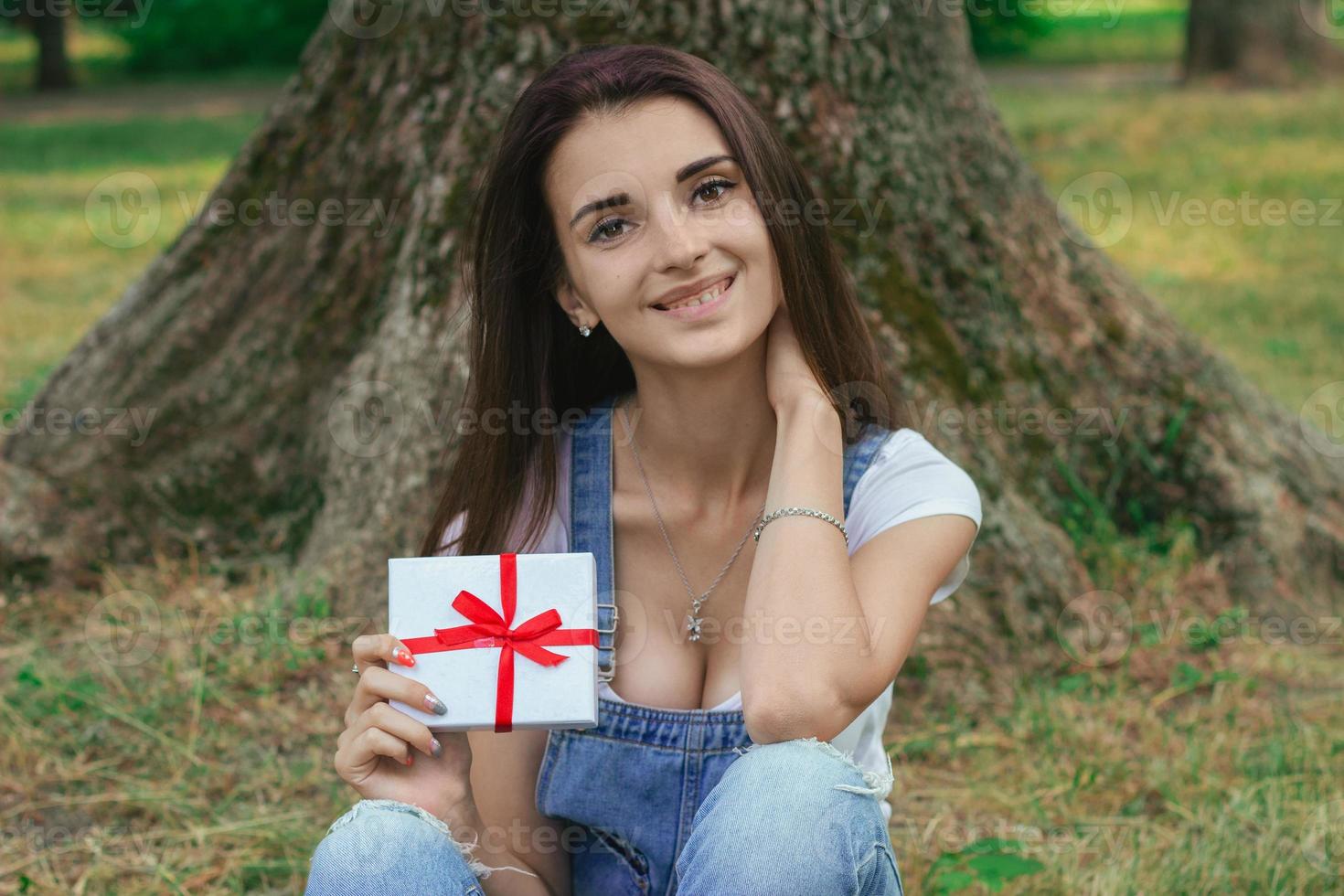 glad ung flicka på de parkera med närvarande i henne händer leende på kamera foto