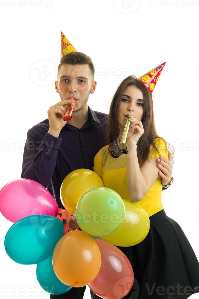 ung kille och Söt flicka blåsa horn och bärande färgad ballonger foto