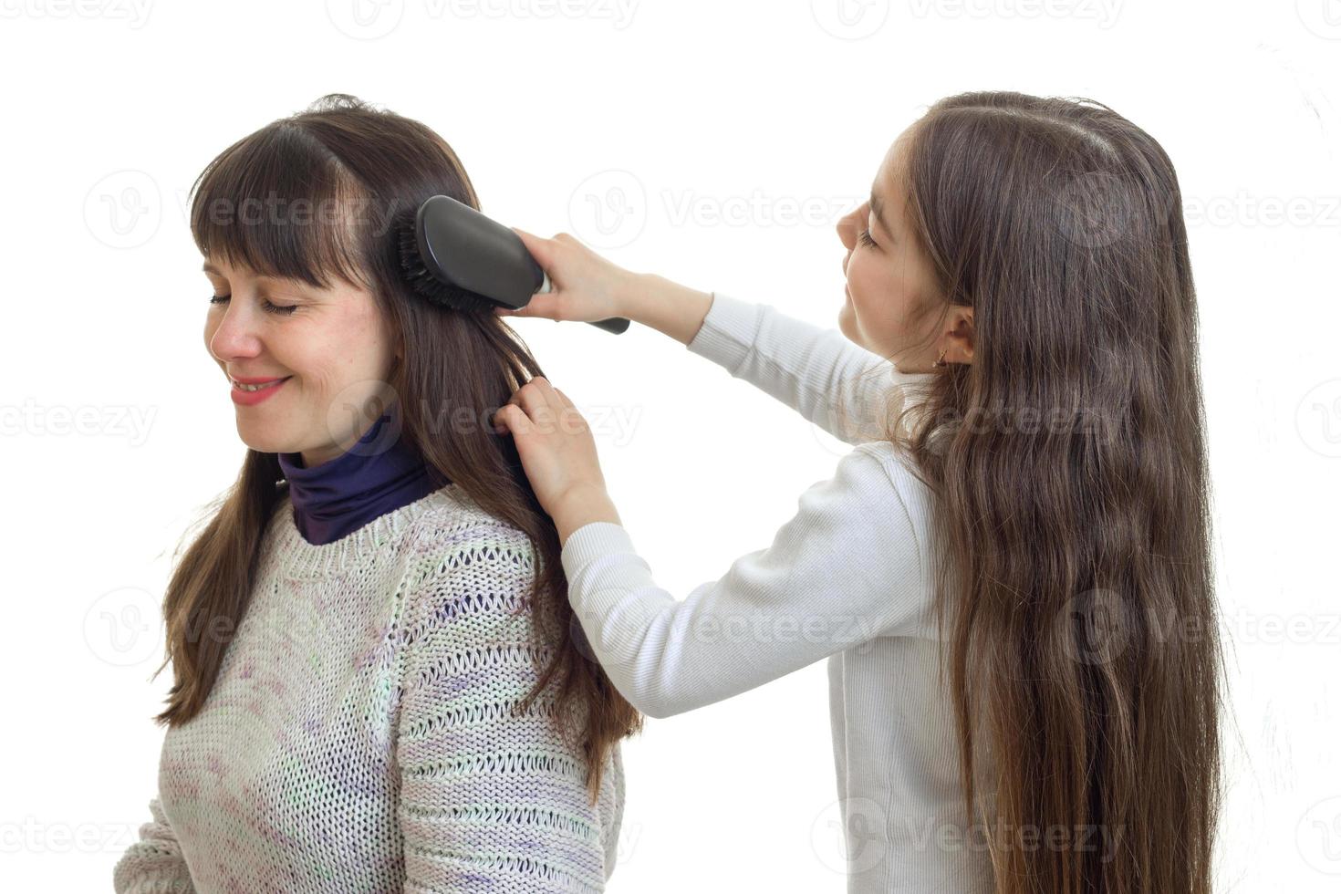 liten flicka coms hår av henne mor i studio foto