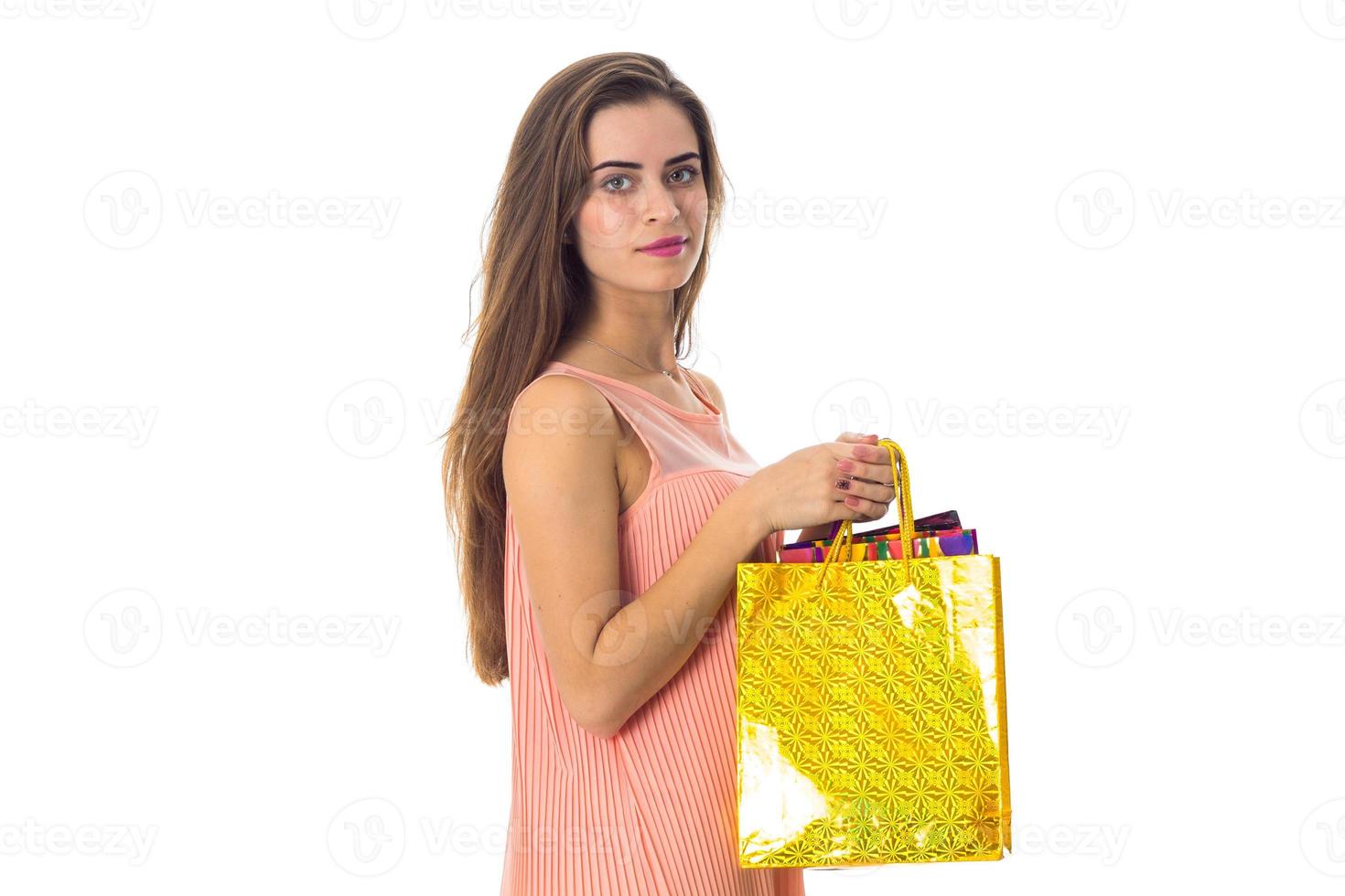 ung flicka står sidled och innehav stor gul paket izoliovano på vit bakgrund foto