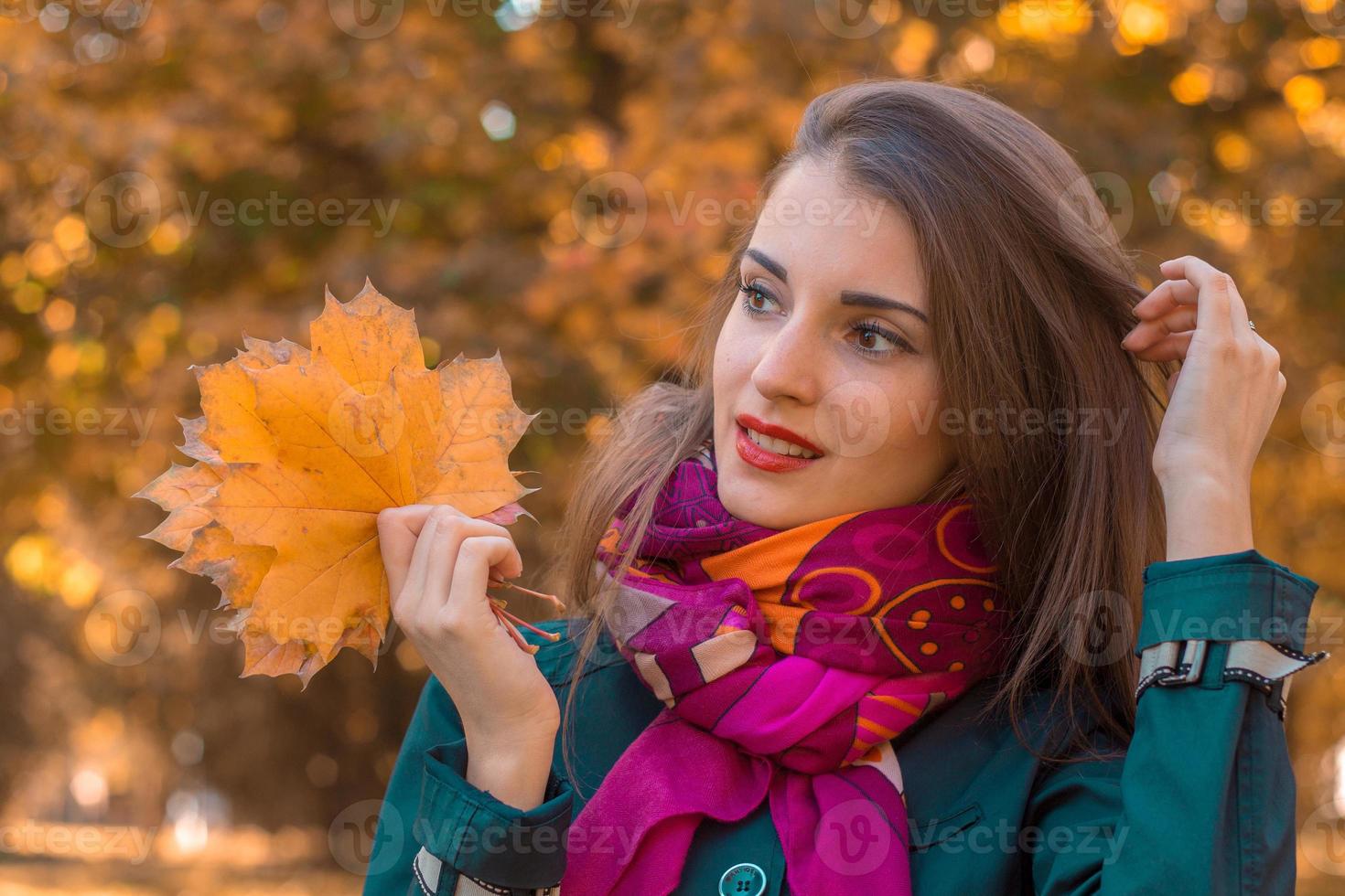 ung flicka i höst parkera utseende till de sida och innehav en orange löv foto