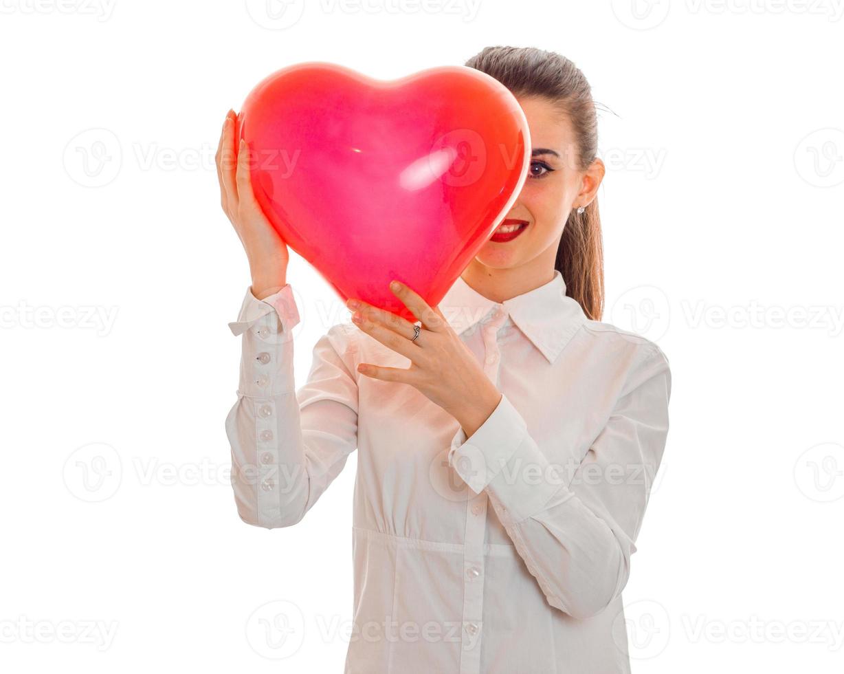 ung Lycklig kvinna med röd mun framställning till fira valentines dag med hjärta symbol i studio isolerat på vit bakgrund foto