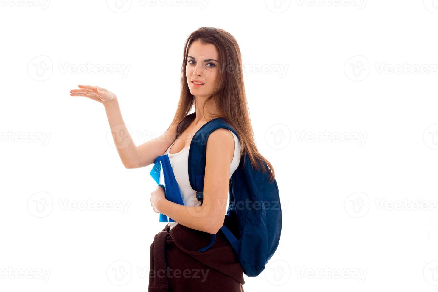 ung missnöjd brunett studerande flicka med ryggsäck på henne axlar och böcker i henne händer pekande till de sida och utseende på de kamera isolerat på vit bakgrund foto