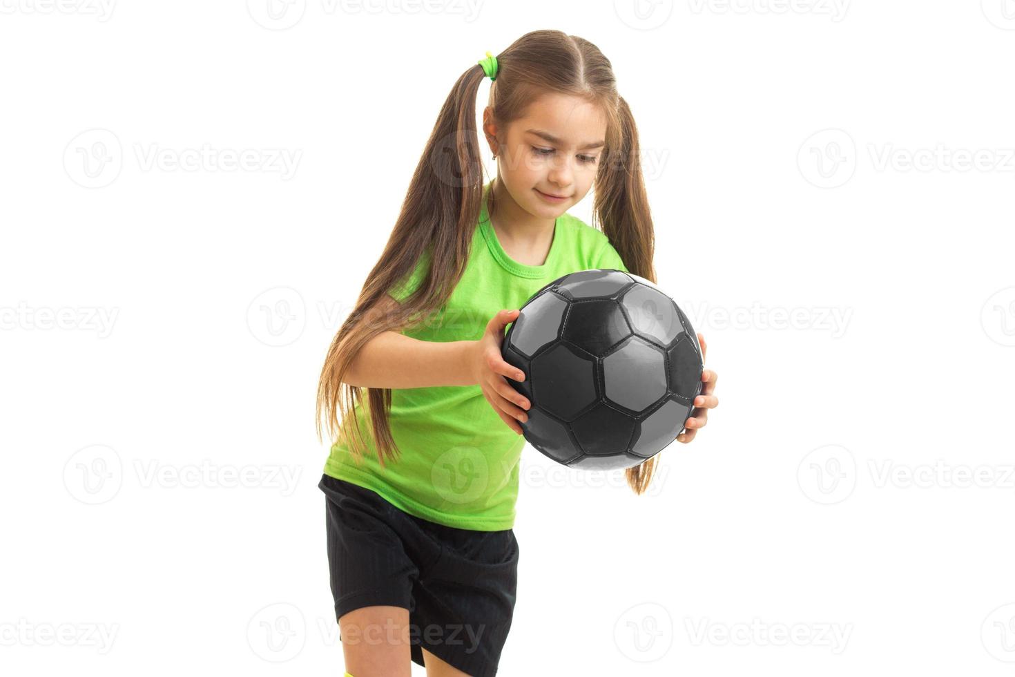 sötnos liten flicka i grön enhetlig med fotboll boll i händer foto