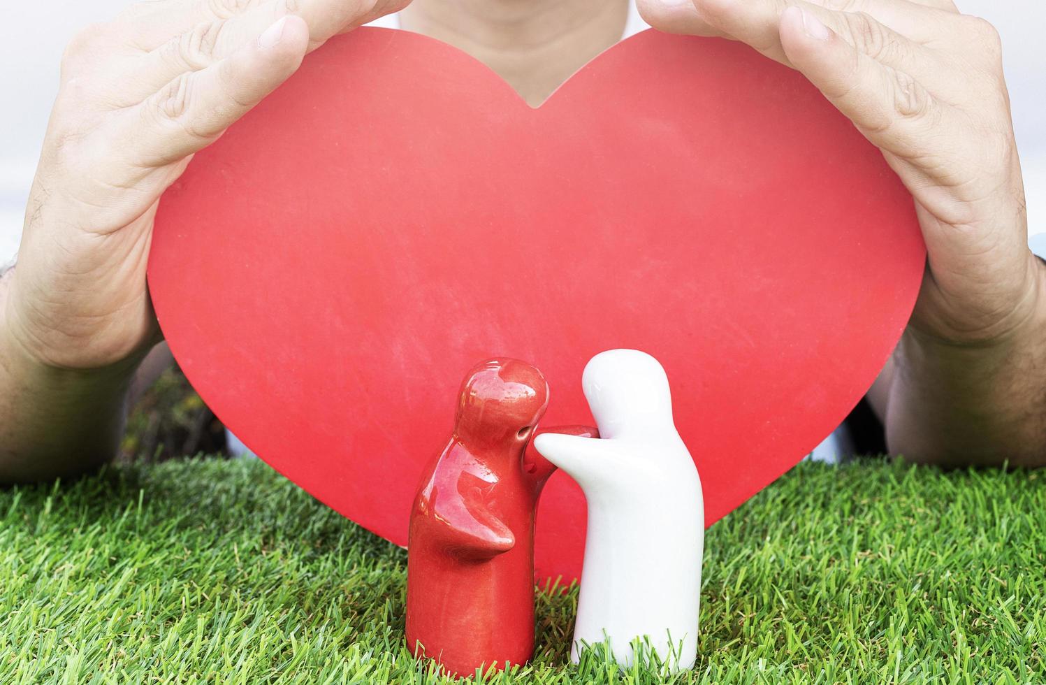 valentine dag begrepp. falsk upp par kramas på gräs golv med hand vakt och röd hjärta bakgrund foto