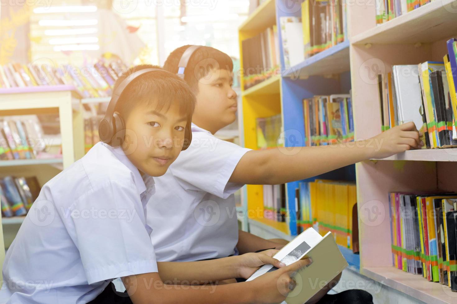 mjuk fucus av två asiatisk pojke studenter är lyssnande media, läsning och hört handla om favorit bok på bibliotek av skola foto