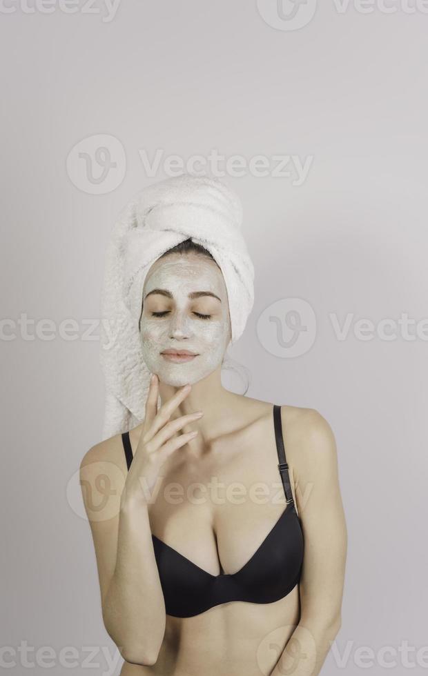 spa kvinna applicering ansiktsbehandling lera mask. skönhet behandlingar. närbild porträtt av skön flicka med en handduk på henne huvud applicering ansiktsbehandling mask. foto