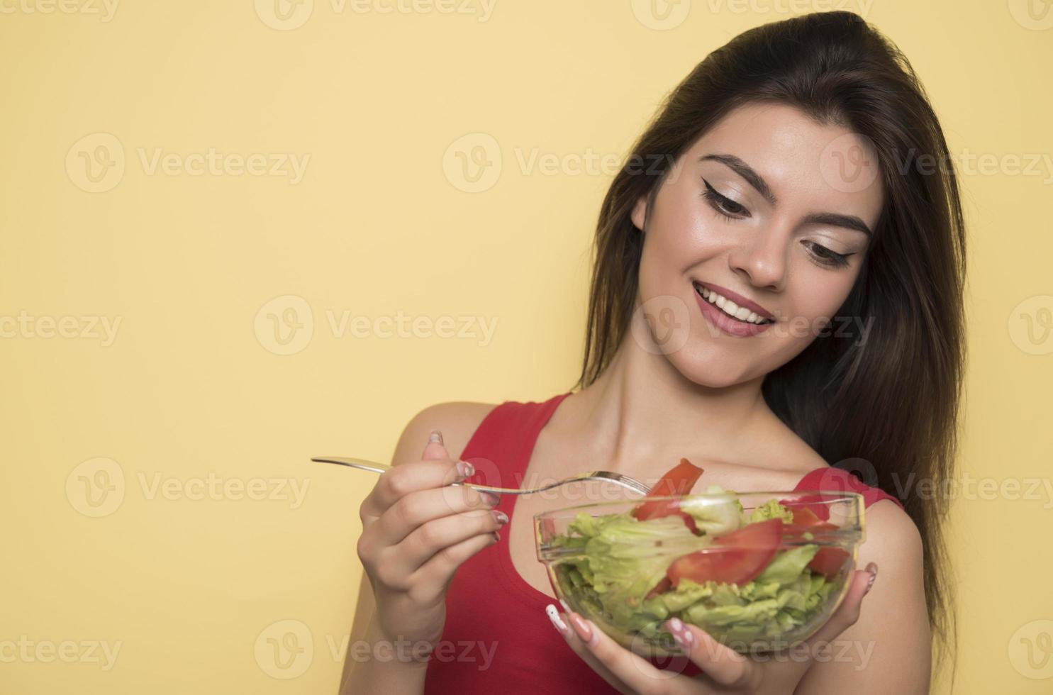 porträtt av en Lycklig lekfull flicka äter färsk sallad från en skål foto