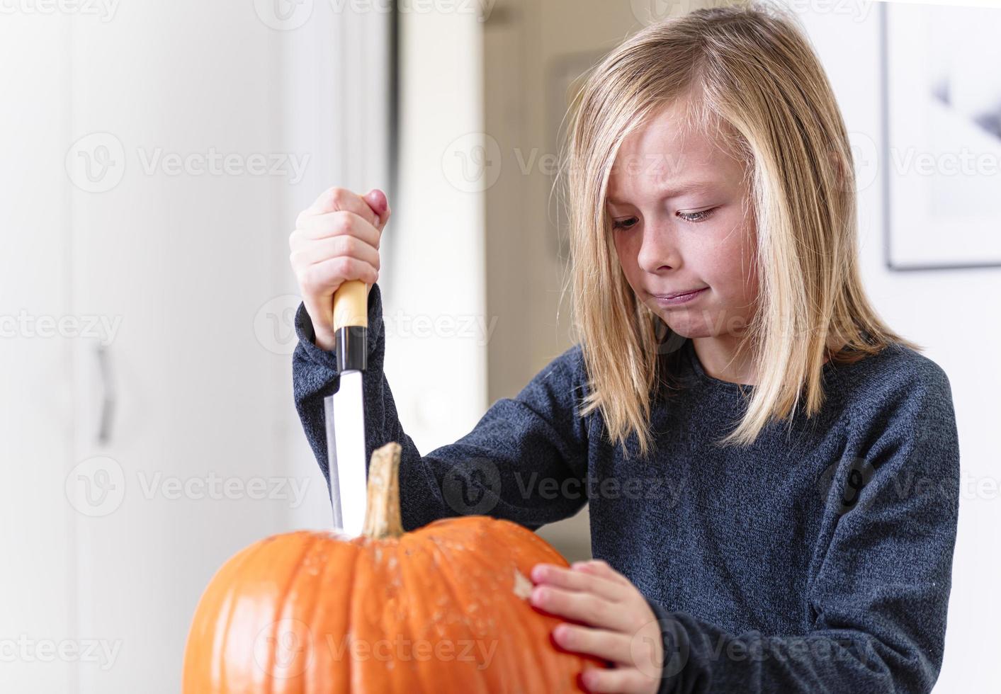 skön blond pojke träsnideri pumpa med kniv för halloween. halloween begrepp foto