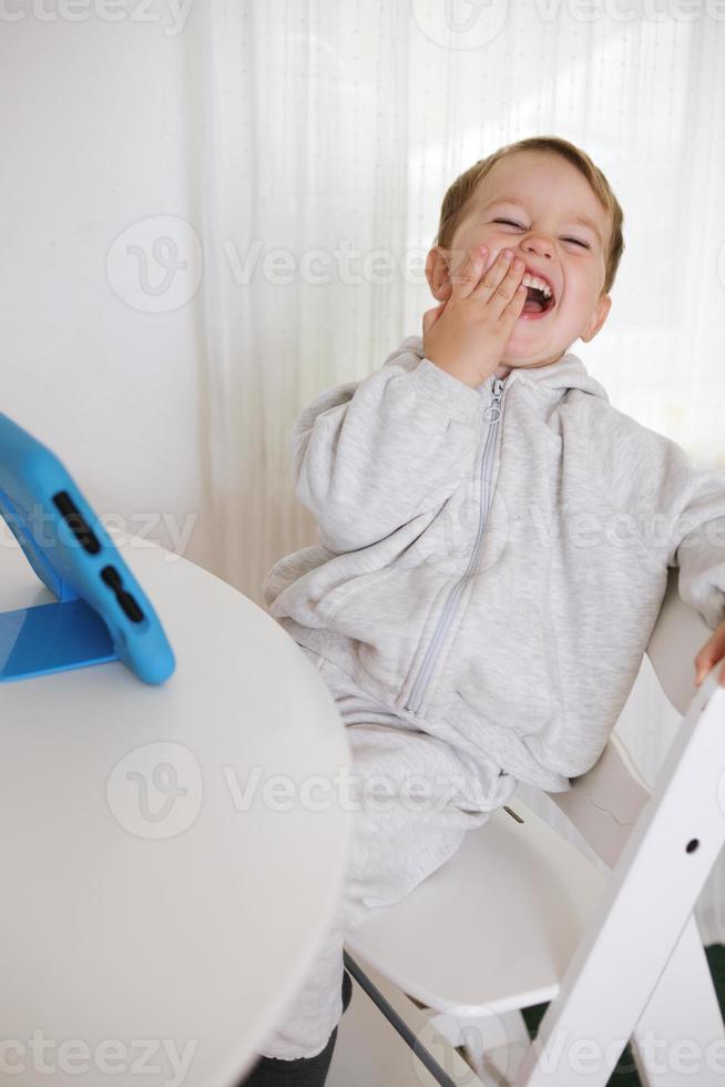 Lycklig liten pojke spelar spel på digital läsplatta på Hem. porträtt av en barn på Hem tittar på tecknad serie på de läsplatta. modern unge och utbildning teknologi. foto