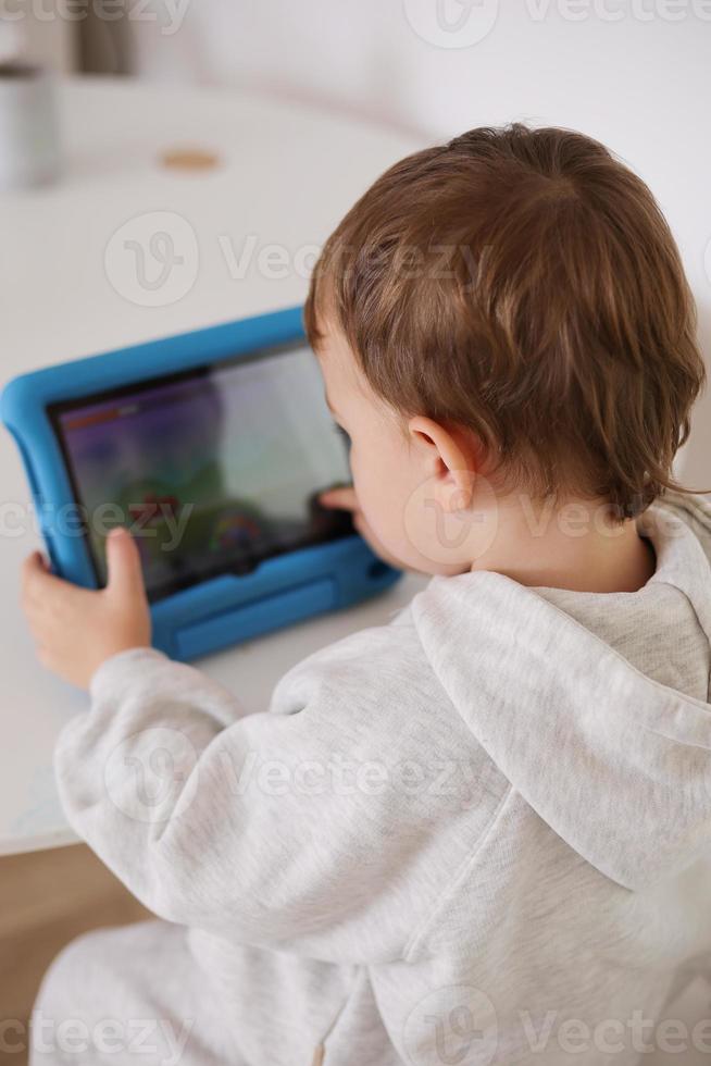 Lycklig liten pojke spelar spel på digital läsplatta på Hem. porträtt av en barn på Hem tittar på tecknad serie på de läsplatta. modern unge och utbildning teknologi. foto