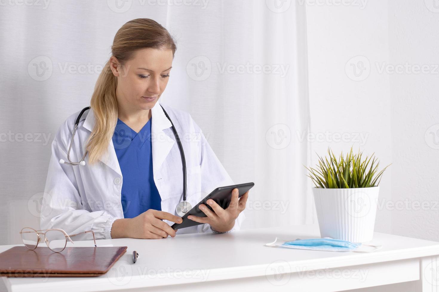 ung kvinna läkare talande med patient uppkopplad med digital läsplatta. samråd, videosamtal, distans. medicin, sjukvård under covid19. läkare med vit täcka, stetoskop, redo till hjälp. foto