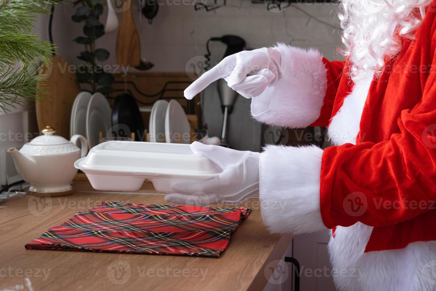 mat leverans till Hem service behållare i händer av santa claus sätter den på kök tabell och tar den bort. färdiggjorda varm ordning, jul, ny år högtider catering. foto