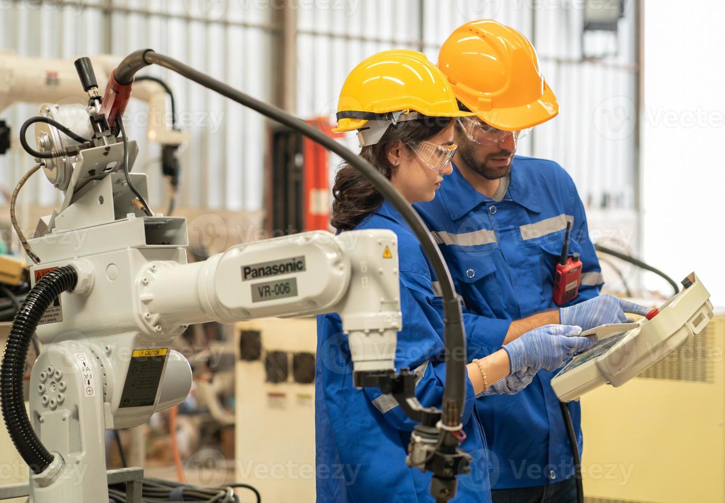 manlig industriell ingenjör använder sig av avlägsen kontrollera styrelse till kolla upp robot svetsare drift i modern automatisering fabrik. kvinna tekniker övervakning robot kontrollant systemet för automatiserad stål svetsning. foto