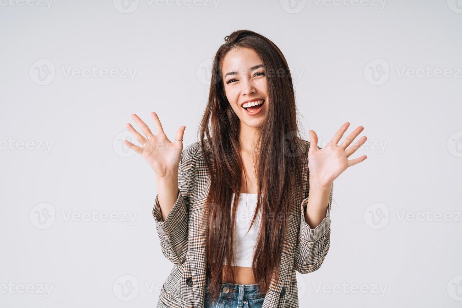 ung Lycklig emotionell asiatisk kvinna med lång hår i kostym på grå bakgrund foto