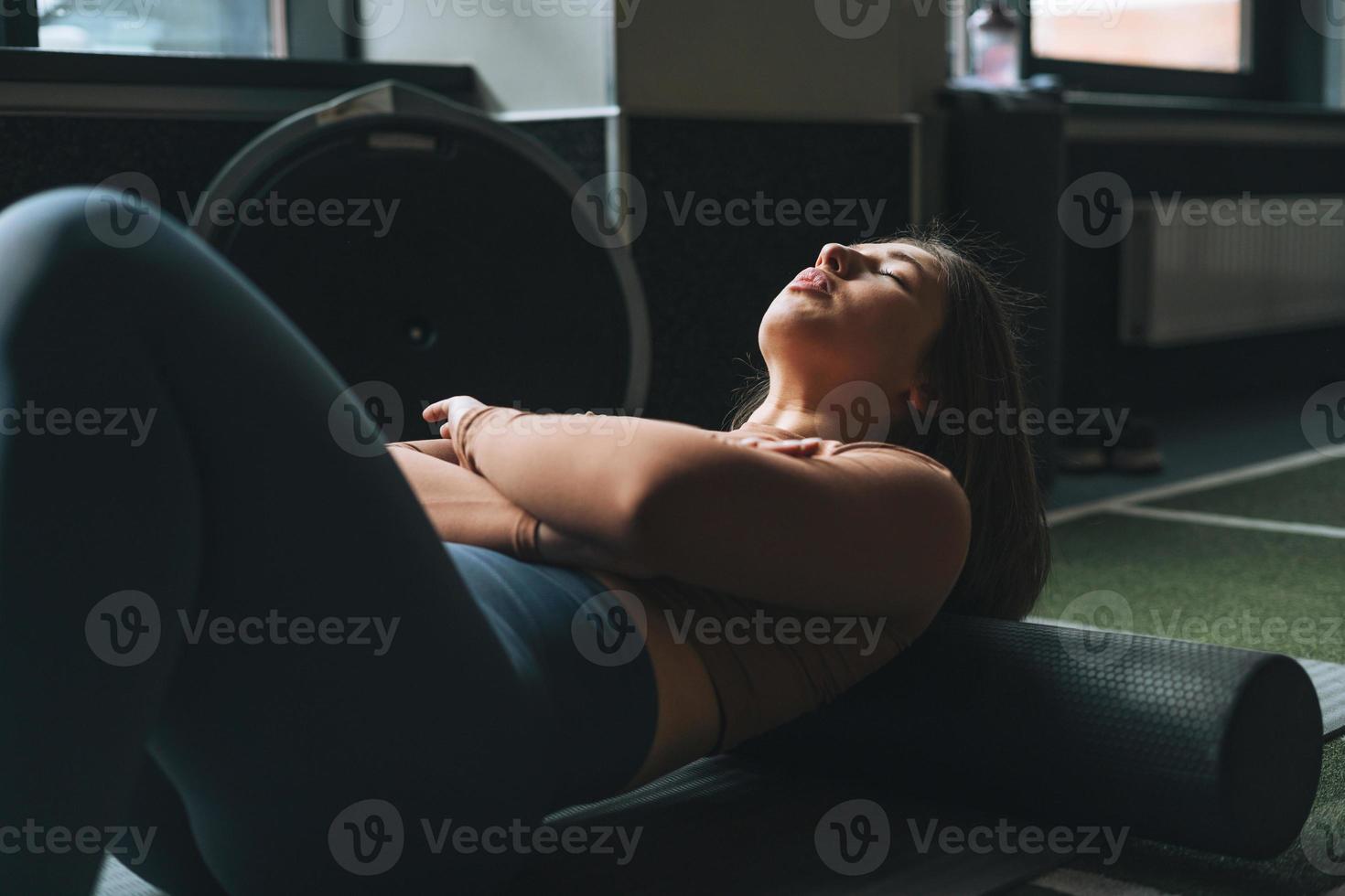 ung brunett kvinna håller på med stretching pilates på massage rulla i de kondition klubb Gym foto