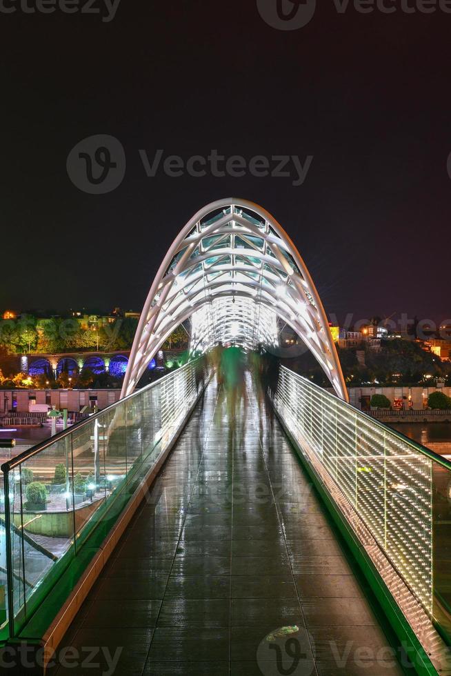 de bro av fred i tbilisi, en fotgängare bro över de mtkvari flod i tbilisi, georgien upplyst på natt. foto