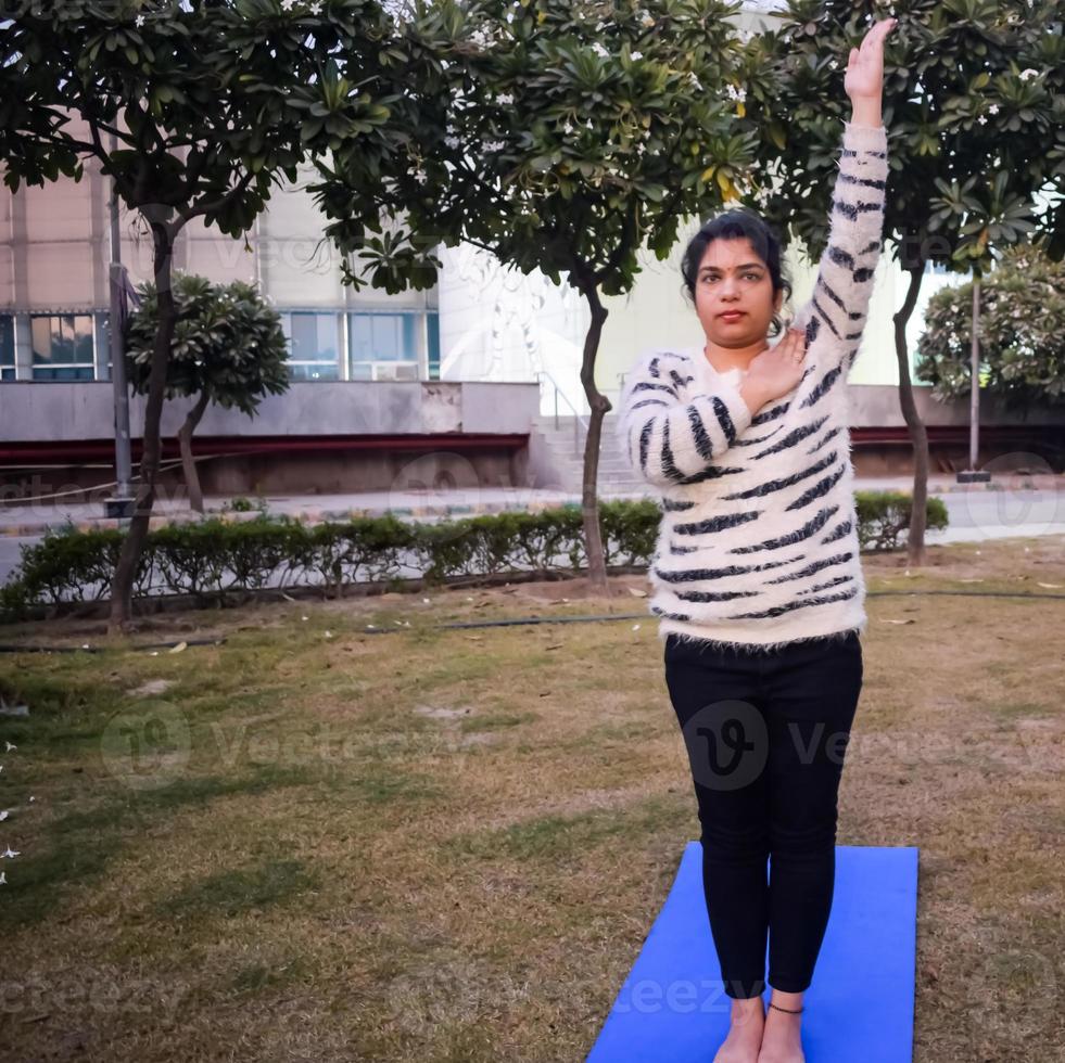 ung indisk kvinna praktiserande yoga utomhus- i en parkera. skön flicka öva grundläggande yoga utgör. stillhet och koppla av, kvinna lycka. grundläggande yoga övning utomhus- foto