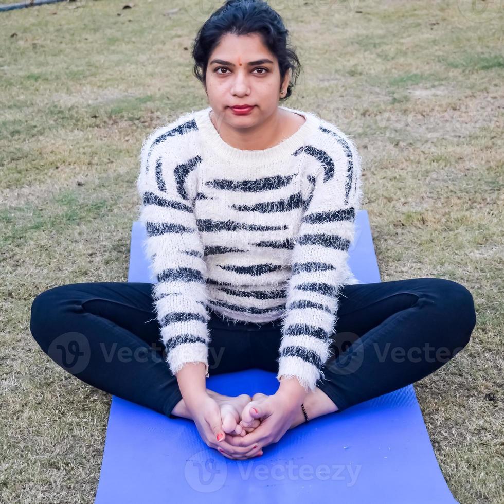 ung indisk kvinna praktiserande yoga utomhus- i en parkera. skön flicka öva grundläggande yoga utgör. stillhet och koppla av, kvinna lycka. grundläggande yoga övning utomhus- foto