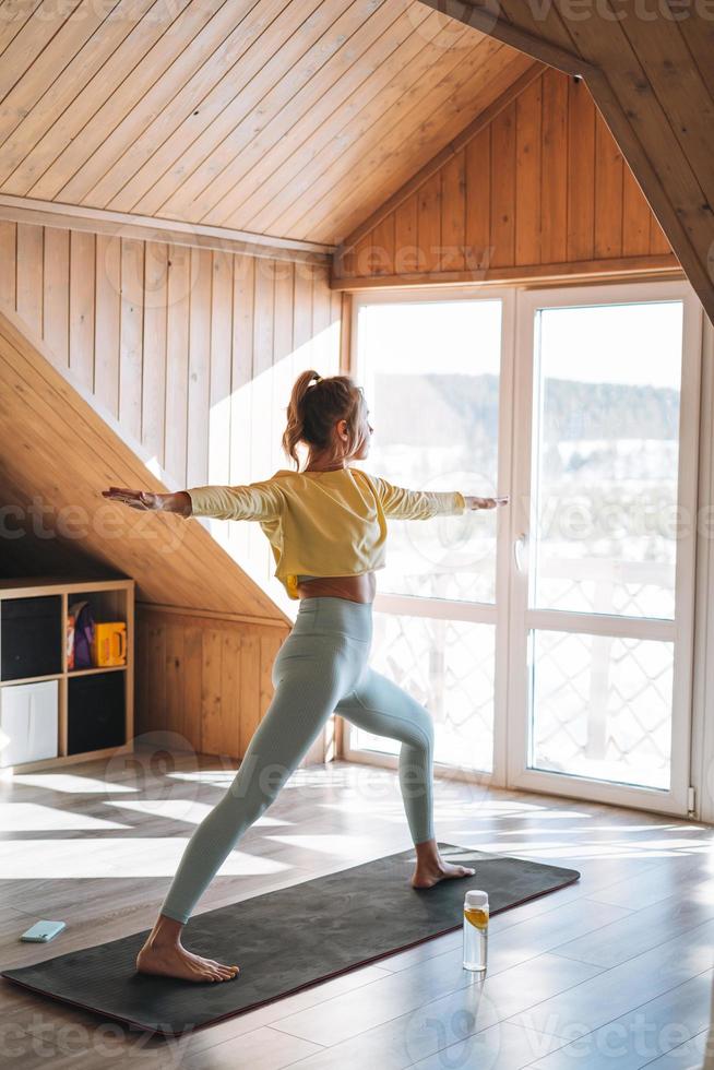 ung slank kondition blond kvinna öva morgon- yoga nära fönster av Hem foto