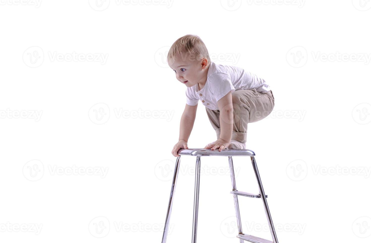 liten pojke klättrar till en stege stol. de början av en karriär begrepp. rolig liten pojke isolerat på vit bakgrund. foto