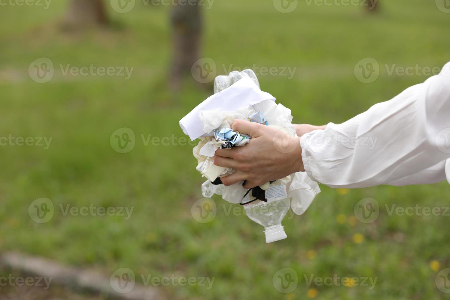 kvinna slänger plastavfall i papperskorgen. kvinna hand plockar upp sopor plast för rengöring i parken. sophämtning efter en pandemi. selektiv fokusering foto