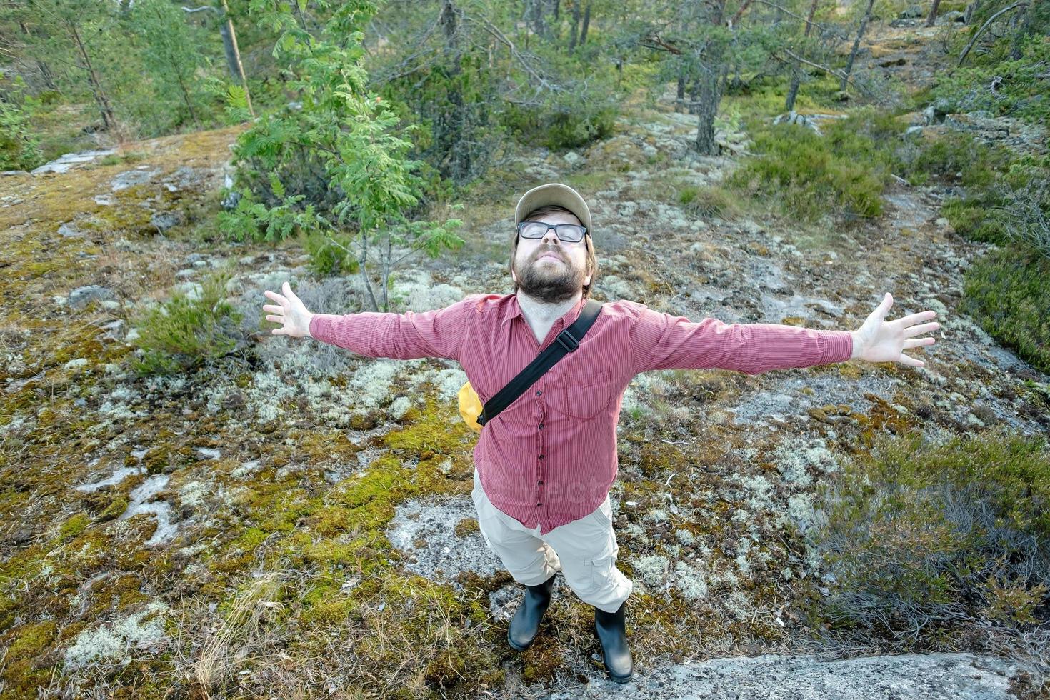 nöjd man glatt spridning hans vapen till de sidor, han är på semester, gående i de skog njuter de färsk luft och natur. foto