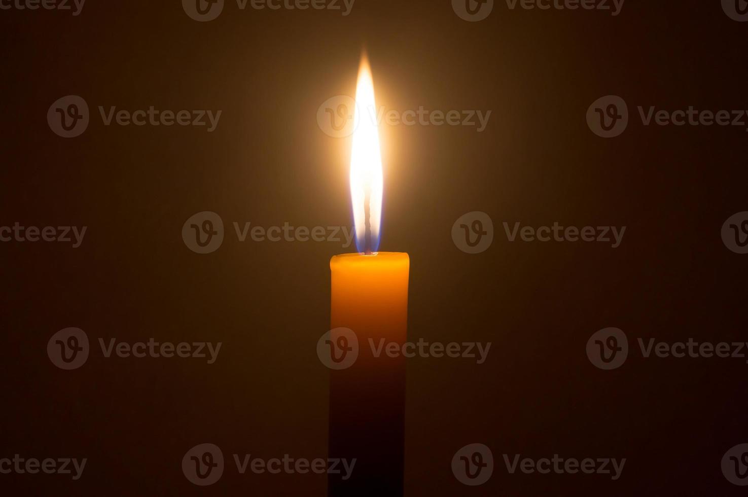 en enda brinnande ljus flamma eller ljus lysande på en gul ljus isolerat på mörk röd bakgrund på tabell i kyrka för jul, begravning eller minnesmärke foto