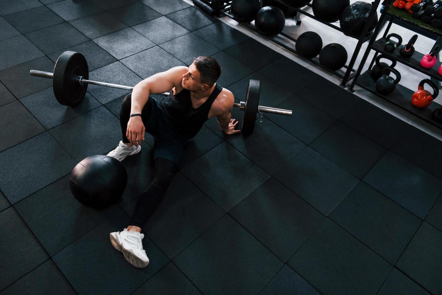 stark man i sportigt kläder Sammanträde på de golv i de Gym med Utrustning foto