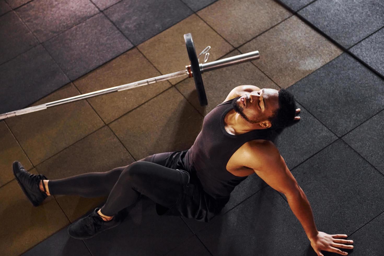 Sammanträde på de golv. stark afrikansk amerikan man i sportigt kläder ha träna dag i de Gym foto