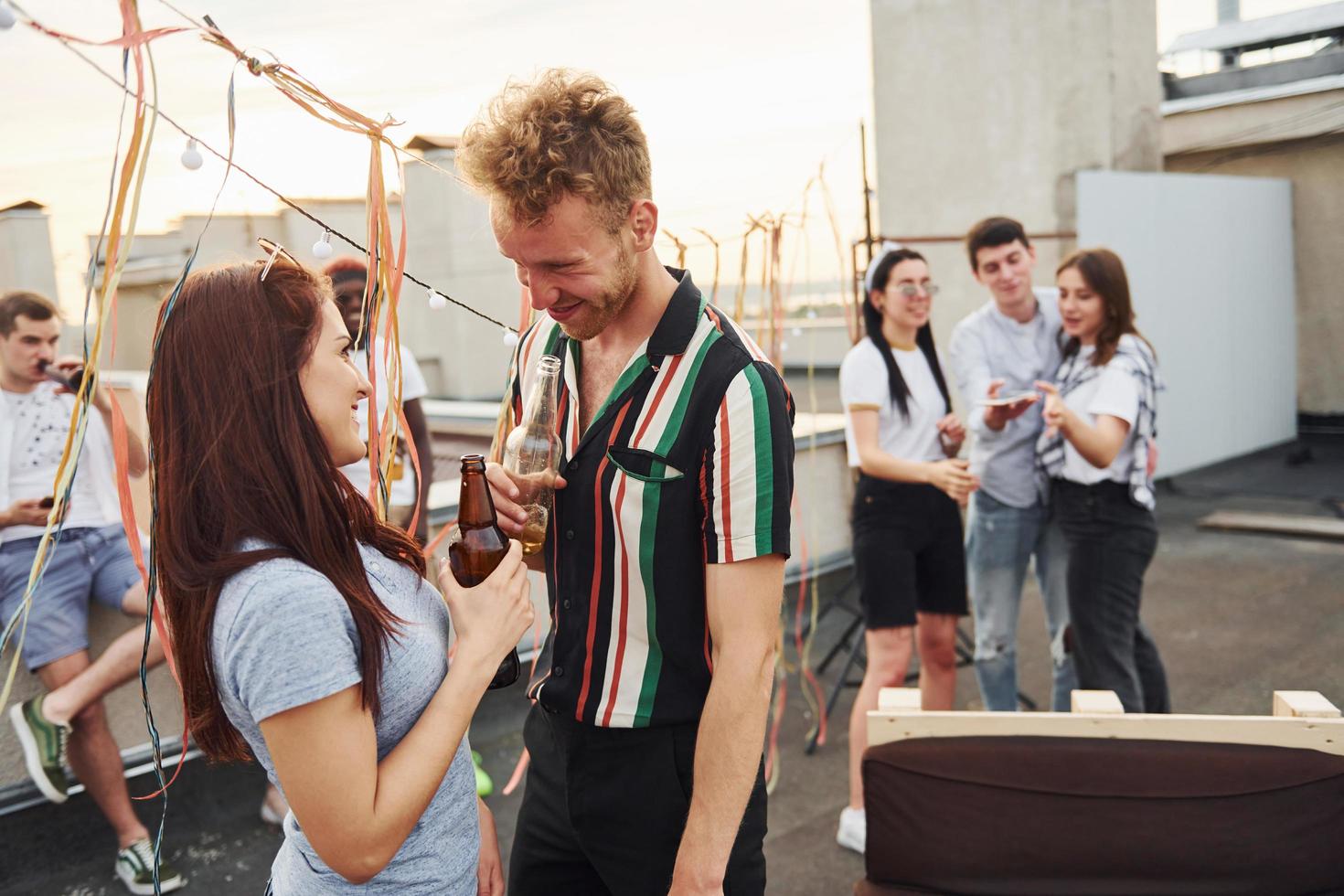 Lycklig par. grupp av ung människor i tillfällig kläder ha en fest på taket tillsammans på dagtid foto