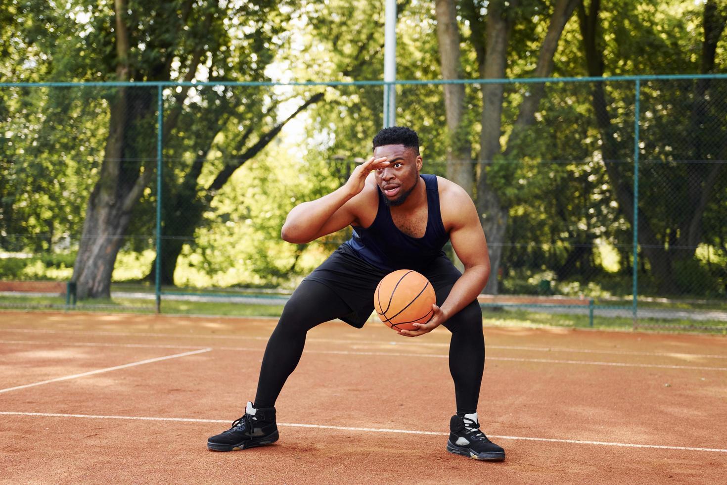 skön grön träd på bakgrund. afrikansk amerikan man spelar basketboll på de domstol utomhus foto