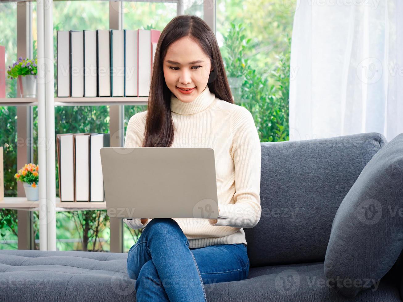 attraktiv ung skön asiatisk kvinnor stanna kvar på Hem med en bärbar dator håller på med forskning arbete för henne företag medan Sammanträde på de soffa i de levande rum. foto