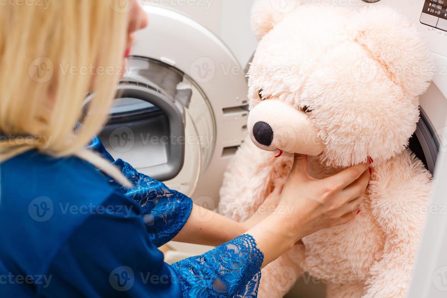 kvinna läser in fluffig leksak i de tvättning maskin foto