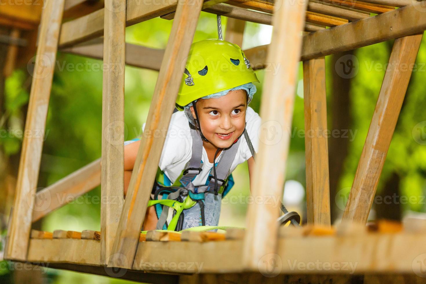 glad skolflicka njuter av aktivitet i en klättrande äventyrspark på en sommardag foto