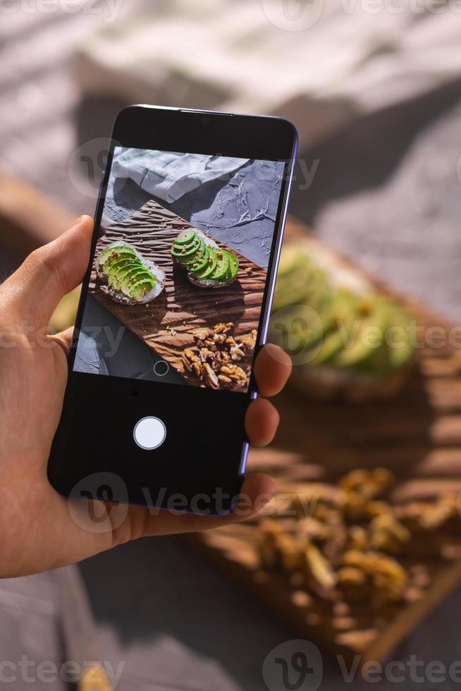smartphone tar bild från organisk friska smörgåsar med avokado. man hand. foto