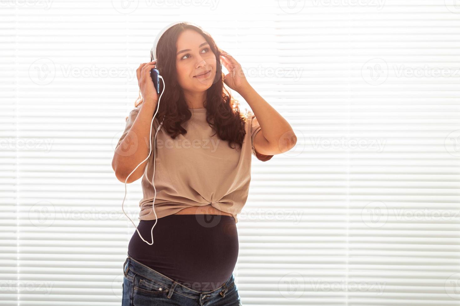 skön ung fredlig gravid kvinna lyssnar till trevlig klassisk musik använder sig av smartphone och hörlurar. begrepp av positiv attityd innan förlossning. kopia Plats foto