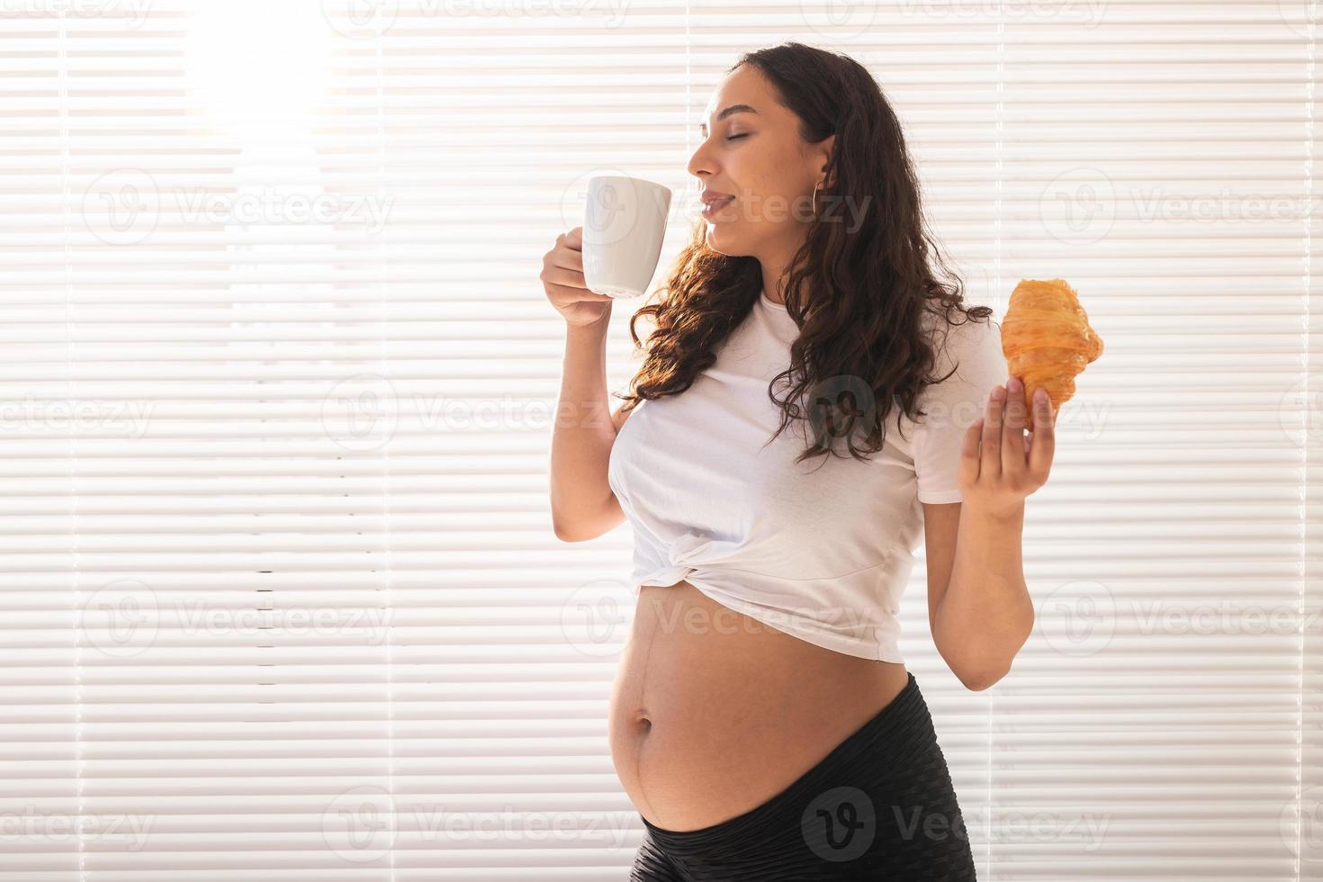 gravid kvinna äter croissant och drycker kaffe. graviditet och moderskap lämna. kopia Plats foto