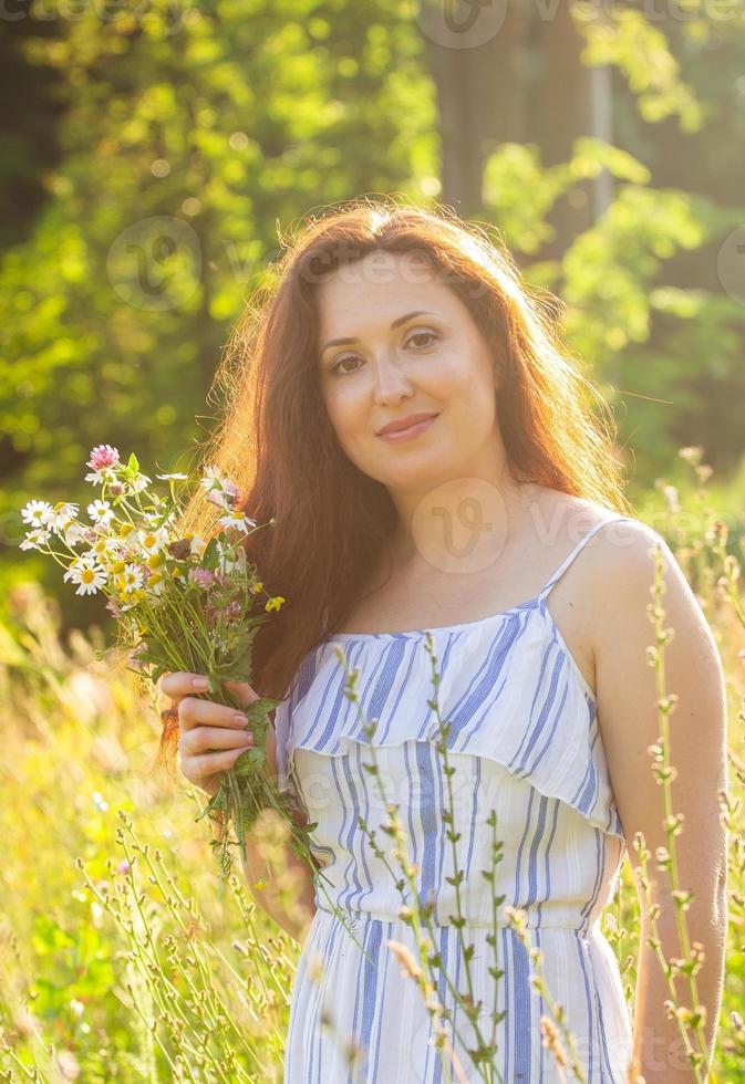 ung kvinna plockning blommor i de äng i sommar kväll foto