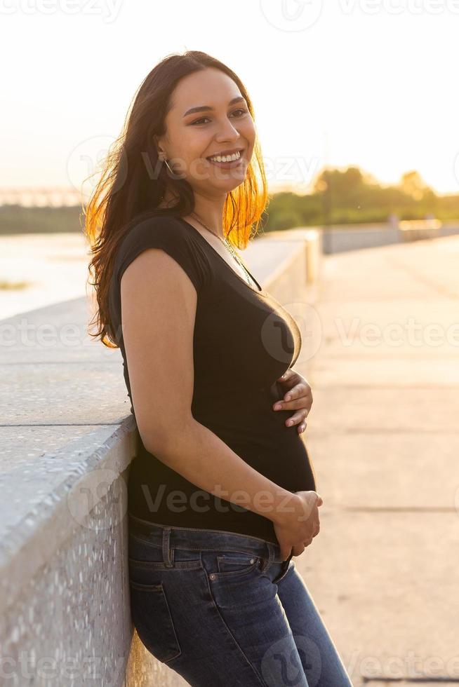 porträtt av latinamerikan gravid kvinna gående på vägbank på solnedgång. graviditet och moderskap begrepp. foto