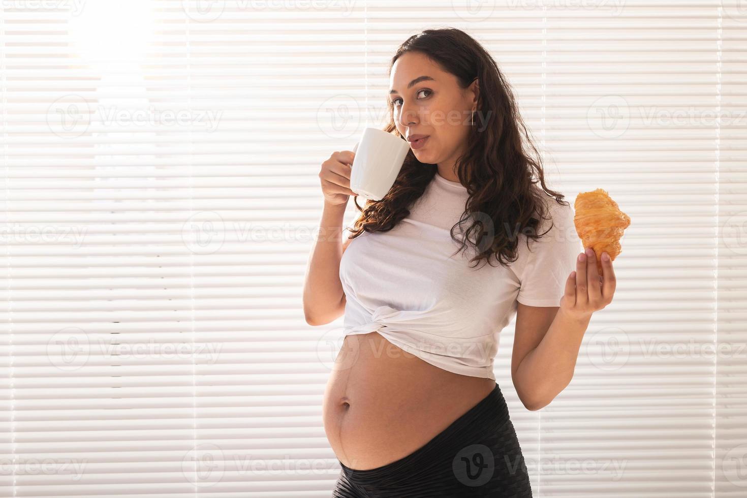 gravid kvinna äter croissant och drycker kaffe. graviditet och moderskap lämna. kopia Plats foto