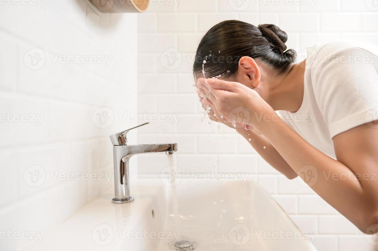 skön asiatisk kvinna är tvättning henne ansikte i badrum på Hem foto